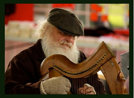Man with white hair and beard wearing a cap and gloves plays a harp