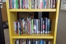 Yellow rolling cart with 3 shelves containing a selection of books for kids and teens
