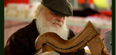 Man with white hair and beard wearing a cap and gloves plays a harp